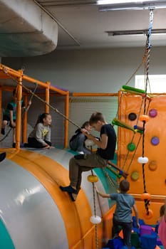 Ivano-Frankivsk, Ukraine June 7, 2023: A child rides on a rope over a pool of soft cubes, children's entertainment in a playroom.