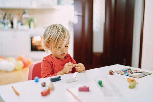 Little girl sits at a table and sculpts from plasticine. High quality photo