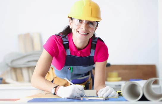 Smiling female construction worker in yellow helmet bent over blueprints. Development of design projects concept