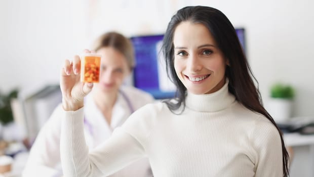Smiling female patient holding pills in background of doctor. Prescribing antidepressants concept