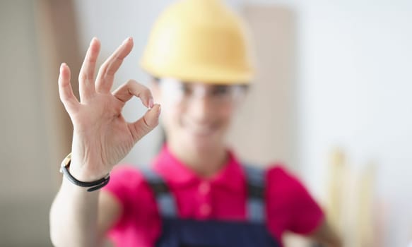 Smiling woman builder holds thumbs up in gesture ok. Housing construction concept