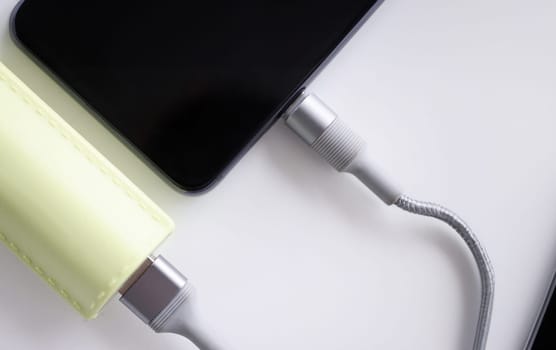 Mobile phone is connected with cable to power bank closeup. Charging mobile devices concept