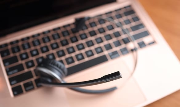 Black head set lying on laptop keyboard closeup. Hot line concept