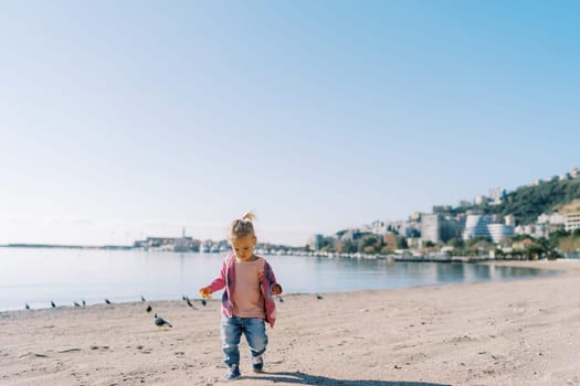 Little girl walks along the sandy beach looking at her feet. High quality photo