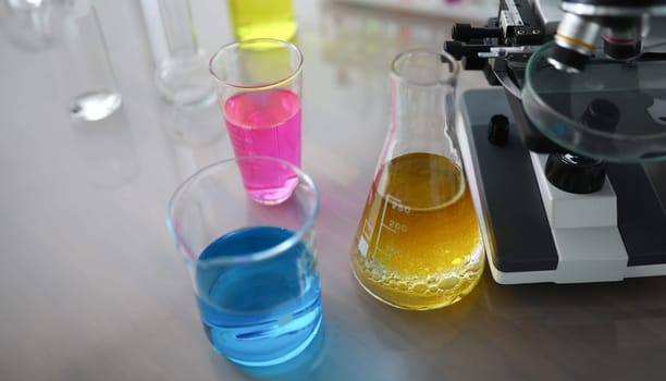Chemical test tubes with multicolored liquid standing near microscope. Laboratory research concept