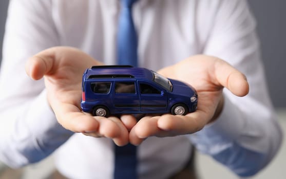 Man holding blue toy car in his hands closeup. Car insurance concept
