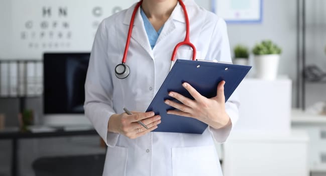 Woman doctor holding clipboard with documents in her hands closeup. Health insurance concept