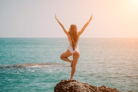 Woman sea yoga. Back view of free calm happy satisfied woman with long hair standing on top rock with yoga position against of sky by the sea. Healthy lifestyle outdoors in nature, fitness concept