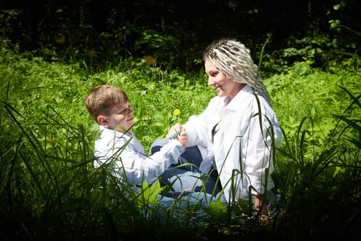 Funny mother with dreadlocks and fat boy happy walking in the forest on a sunny summer day