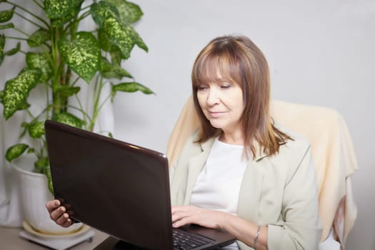 Elderly lady with a laptop in the room. A businesswoman is a leader, a manager is working. Grandma communicates with her grandchildren on the Internet