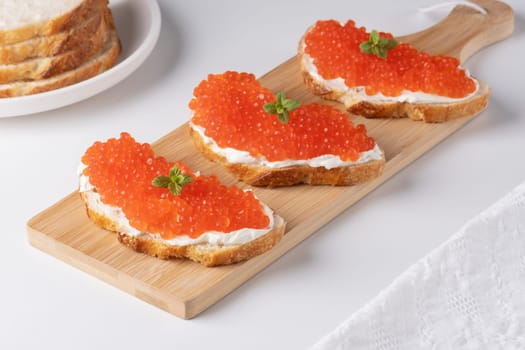 Three sandwiches with red caviar on a cutting board. A delicious appetizer of trout caviar on a slice of bread with cream cheese. Salted salmon caviar for fish delicacy concept.