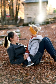 Little girl sits on her mother stomach lying on fallen leaves in the forest. High quality photo