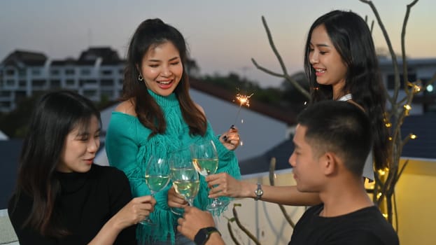 Group of cheerful young people having fun during a rooftop party while toasting with alcohol