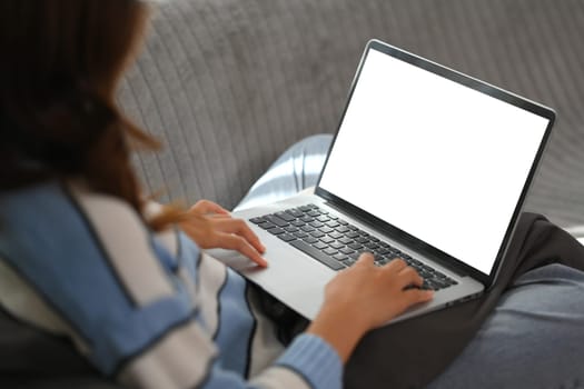 Cropped shot young woman using laptop on comfortable couch at home. Blank screen for advertising