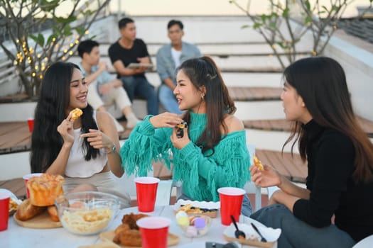 Group of cheerful friends having fun talking and drinking at party on rooftop party.