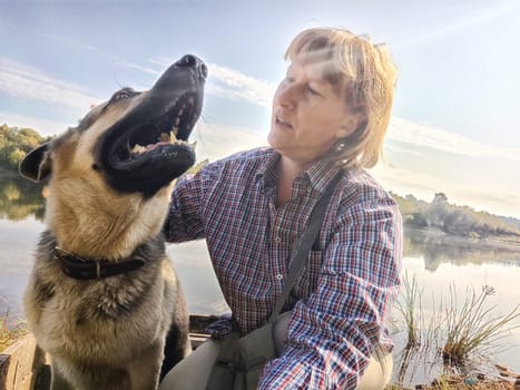 Adult girl with shepherd dog taking selfie in forest. Middle aged woman and big shepherd dog on nature. Friendship, love, fun, hugs