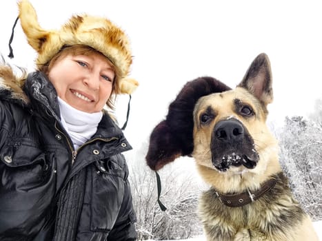 Funny Adult girl with shepherd dog in fur caps taking selfie in winter cold nature. Middle aged woman and big pet in Christmas or New Year time