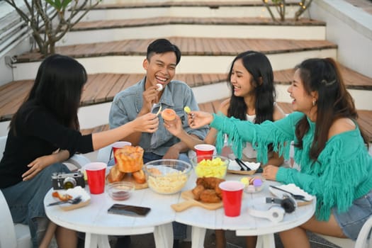 Group of cheerful friends having fun talking and drinking at party on rooftop