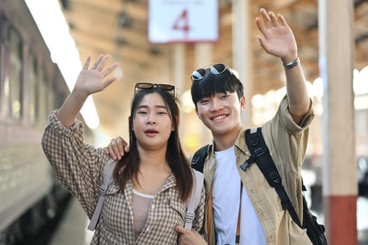 Cheerful young couple greeting a friends at railway station after arrival. Traveling and vacations concept.