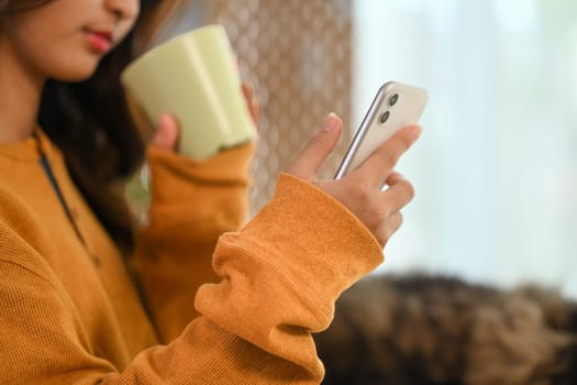 Cropped shot young woman drinking tea and reading message on mobile phone