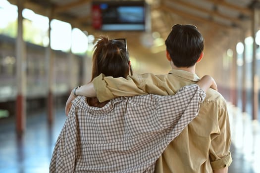 Young necking couple walking along platform at a railway station. Traveling and vacations concept.