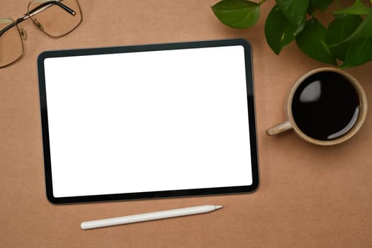Top view digital tablet with white empty screen, coffee cup and glasses on brown background.