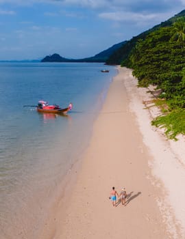 A beautiful view of a couple walking on a calm beach with crystal clear water on the blue sky at Koh Libong, Trang province, Thailand, Andaman Sea. A couple of men and woman walking on the beach