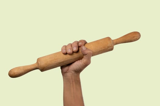 Hand holding a wooden rolling pin isolated on light green background. High quality photo