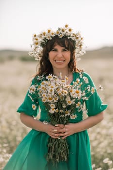 Happy woman in a field of daisies with a wreath of wildflowers on her head. woman in a green dress in a field of white flowers. Charming woman with a bouquet of daisies, tender summer photo.