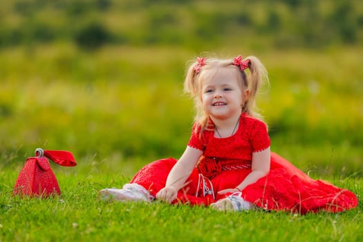 little girl in a red dress sits on a green lawn