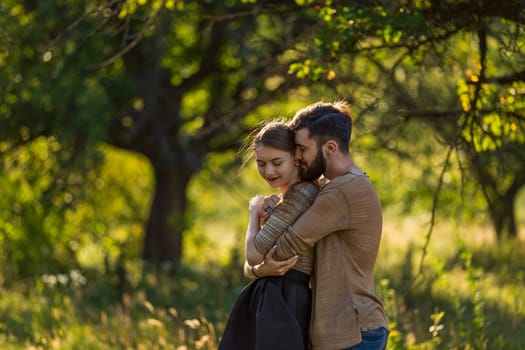 young couple, illuminated by the backlit sun, hugging in nature