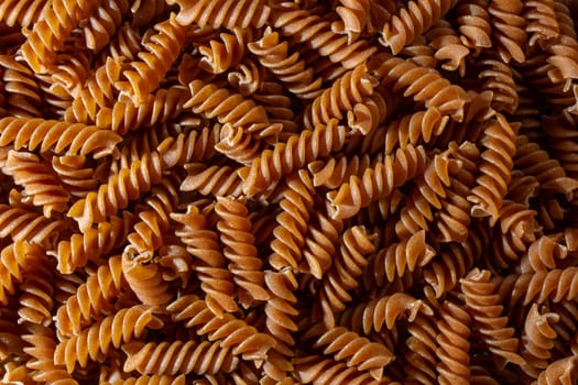 Uncooked Whole Grain Fusilli Pasta: A Culinary Canvas of Whole Wheat Spirals, Creating a Lively and Textured Background for Gourmet Cooking. Whole Grain Twisted Dry Pasta. Whole Wheat Raw Macaroni