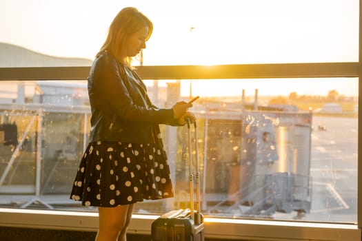 At the airport, under sunlight, a woman is confirming the departure time