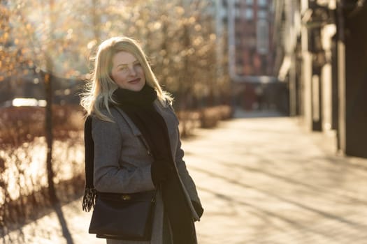 Beautiful young stylish blonde woman wearing long coat walking through the city streets. Trendy casual outfit. Street fashion. . High quality photo