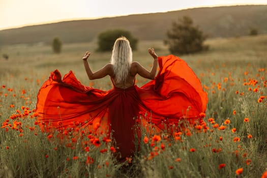 Woman poppy field red dress sunset. Happy woman in a long red dress in a beautiful large poppy field. Blond stands with her back posing on a large field of red poppies.