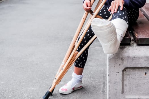 unrecognizable girl sits on the street on a bench with a broken leg and crutches