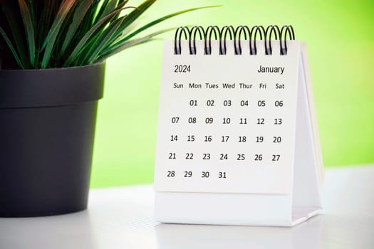 January 2024 desk calendar with potted plant on a desk with green background. Copy space.