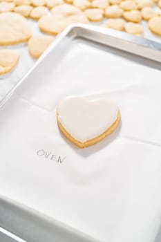 Decorating heart-shaped sugar cookies with pink and white royal icing for Valentine's Day.