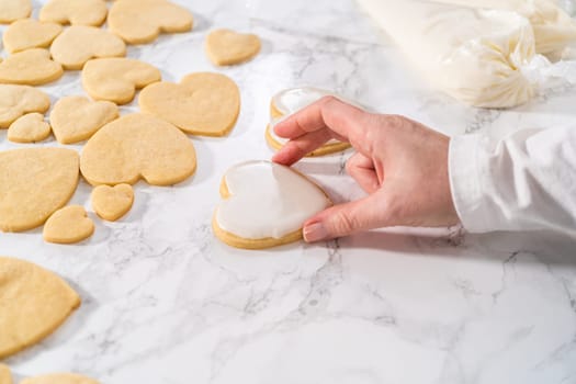 Decorating heart-shaped sugar cookies with pink and white royal icing for Valentine's Day.