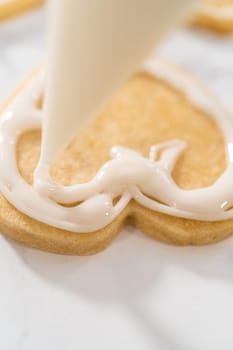 Decorating heart-shaped sugar cookies with pink and white royal icing for Valentine's Day.