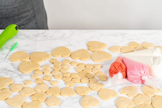 Decorating heart-shaped sugar cookies with pink and white royal icing for Valentine's Day.