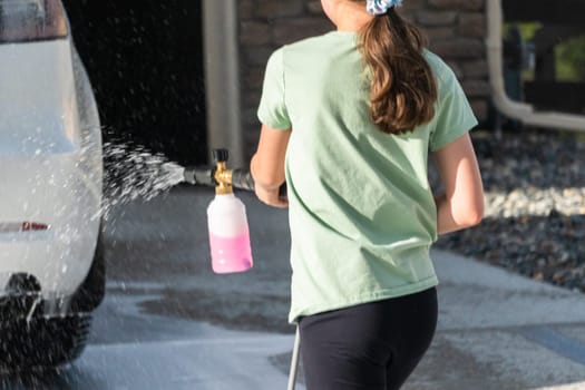 A young girl enthusiastically assists in washing the family's electric car in their suburban driveway.