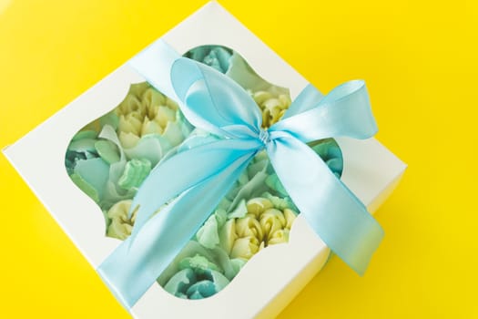Colorful flower arrangement in a white gift box with a window. A bright blue satin ribbon is tied around the box with an elegant bow
