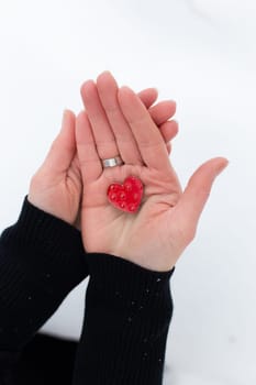 Red heart in the hands of a girl on a light background, it is snowing
