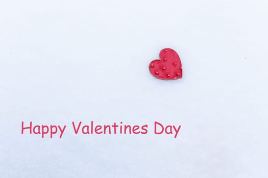 Red heart lies in the snow, holiday concept, lettering Valentine's Day, ready postcard