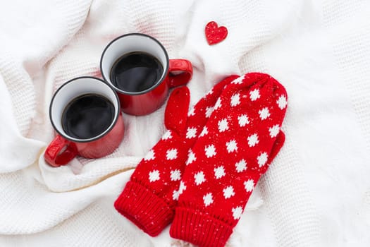 Romantic still life, two red cups of coffee on a white plaid together with red mittens. Valentine's day concept