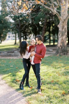 Mom leans over to the little girl in the arms of dad standing in the autumn park. High quality photo