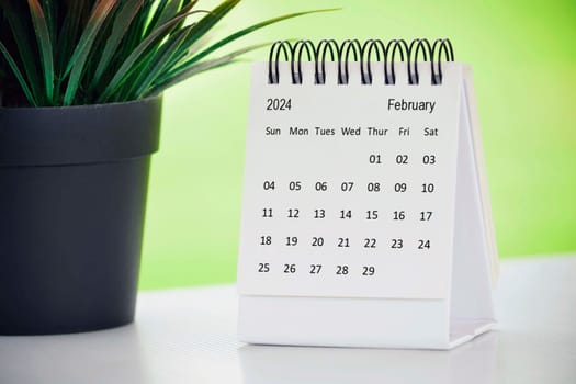 February 2024 desk calendar with potted plant on a desk with green background. Copy space.