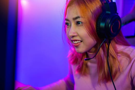 Happy Gamer endeavor plays online video games tournament with computer neon lights, young woman wearing gaming headphones intend to do playing live stream games online at home