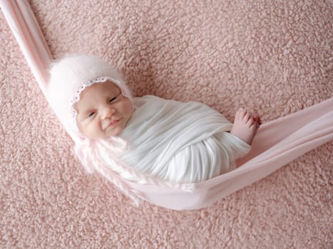 Newborn Baby, Swaddled In A Blanket, Sleeps In A Hammock During A Photo Session With A Smile